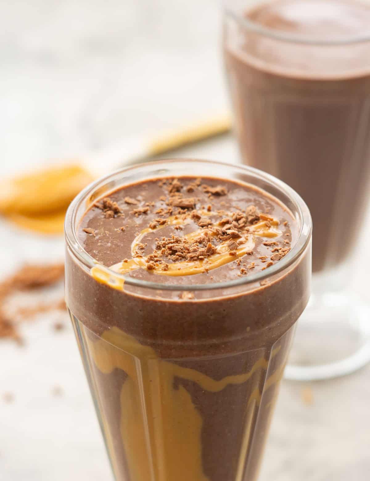 A swirled chocolate and peanut butter smoothie in a tall glass on a marble bench top.