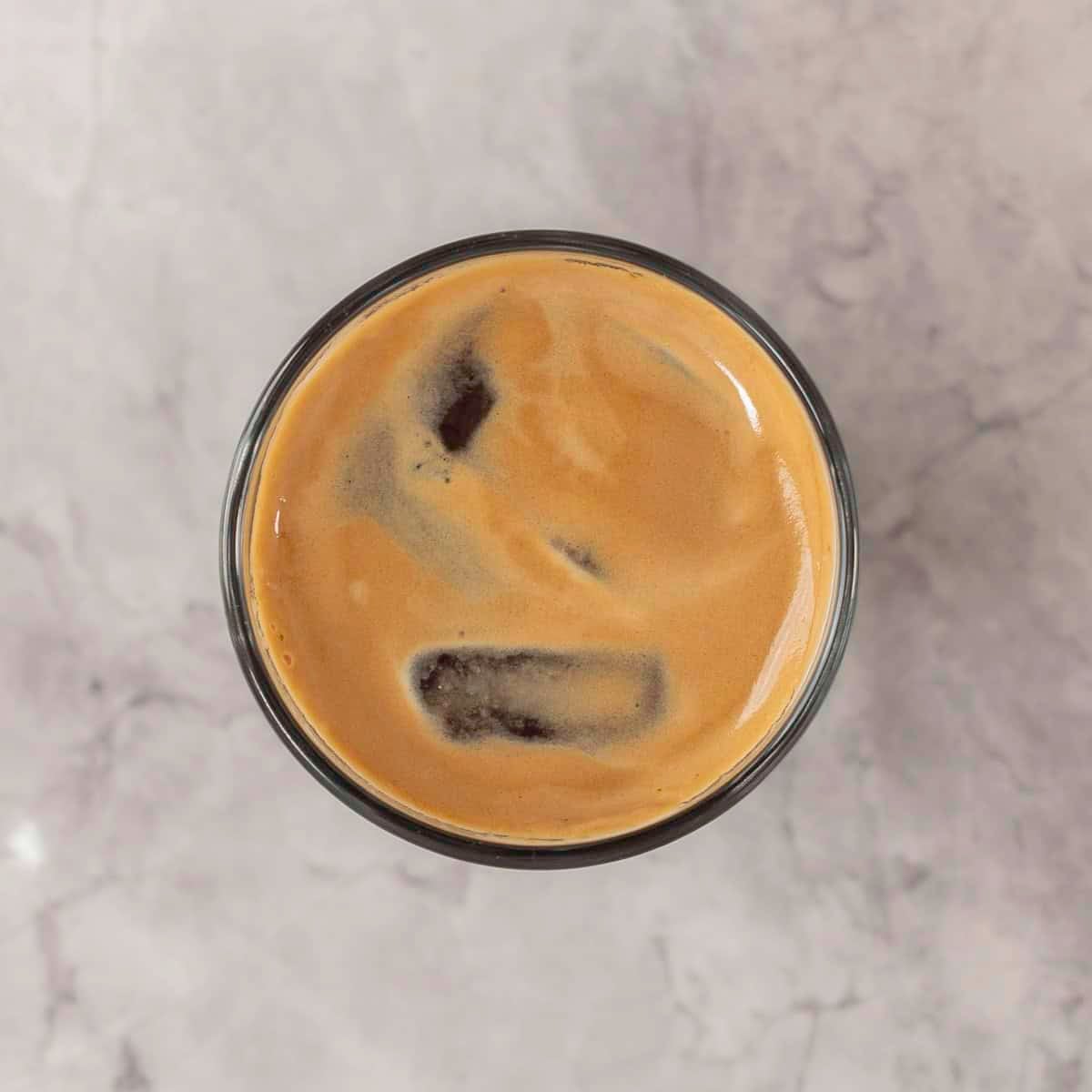 Glass of a shot of coffee on bench with ice cubes in it.