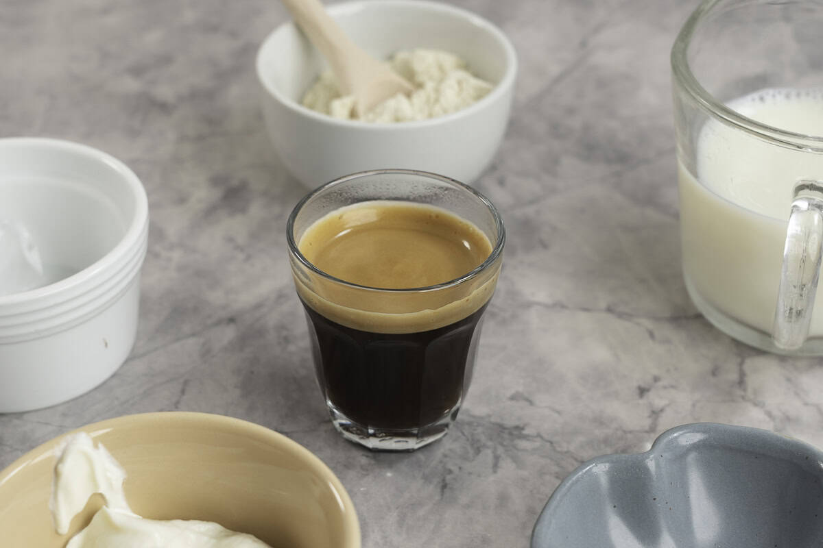 Shot of coffee in a glass on marble bench top with small ramekin surrounding with ingredients for protein shake.