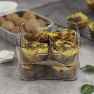 Eight egg muffins stacked in a quart container four on top of one another separated by baking paper.