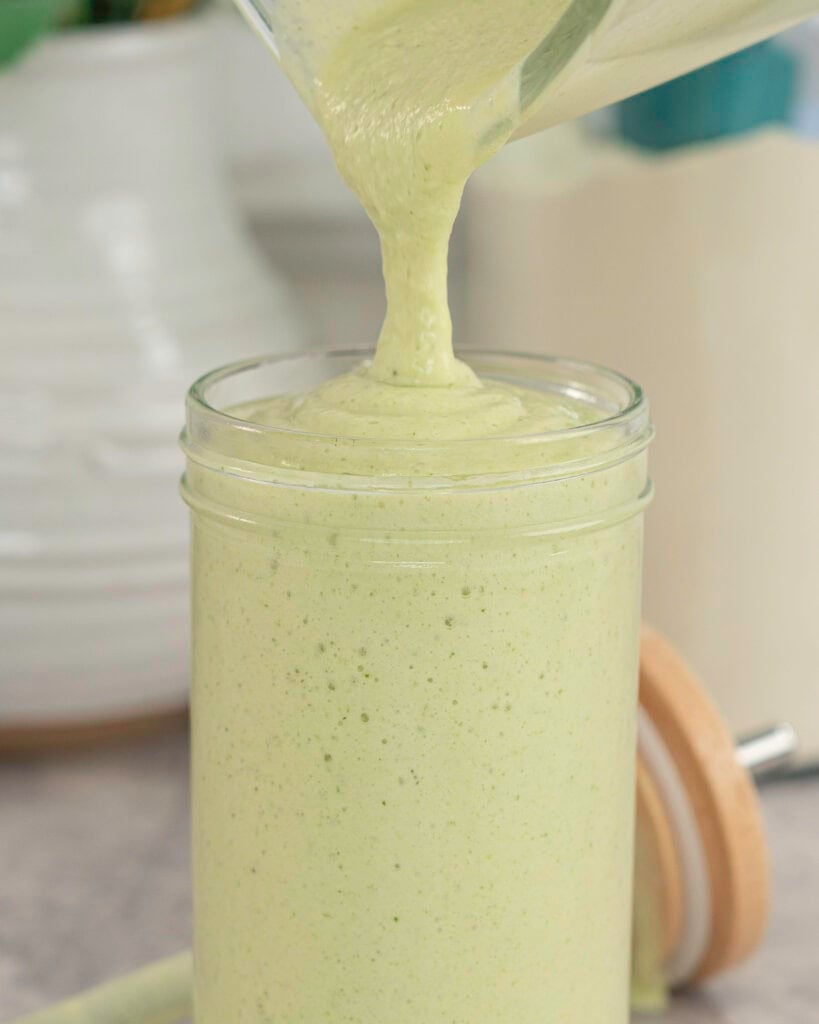 Green creamy smoothie being poured into a large glass.