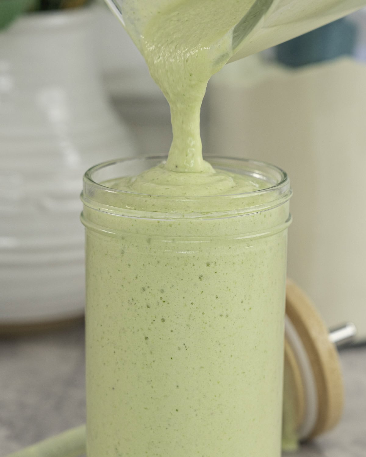 Green creamy smoothie being poured into a large glass.