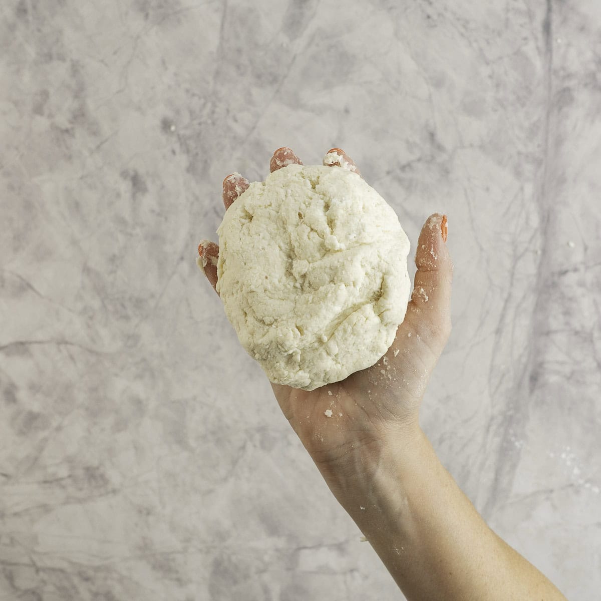 Womans hand holding a round ball of bagel dough in her palm.