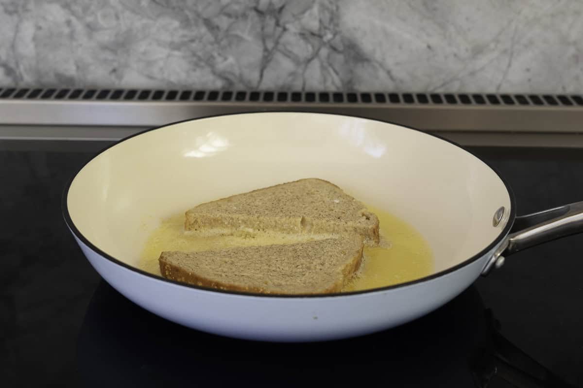 A piece of bread cut into two triangles inside pan with butter inside.