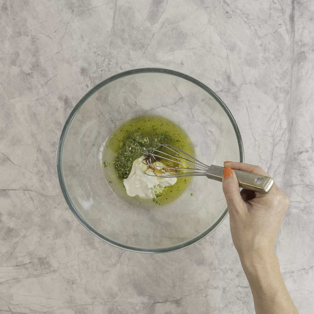 Wet ingredients for pasta salad in a large glass bowl being whisked together.