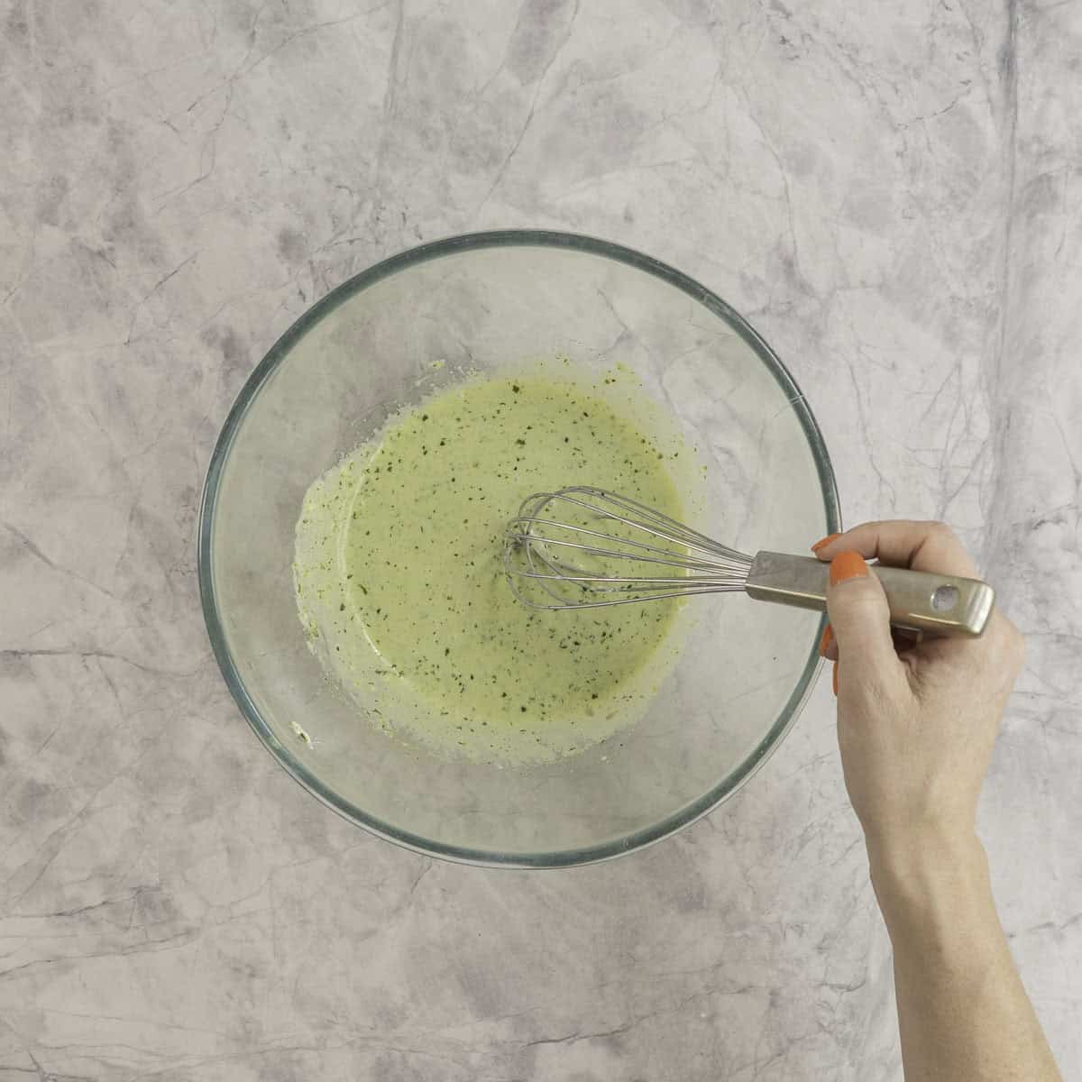 Hand holding a whisk with mixed together wet ingredients in a large glass bowl.