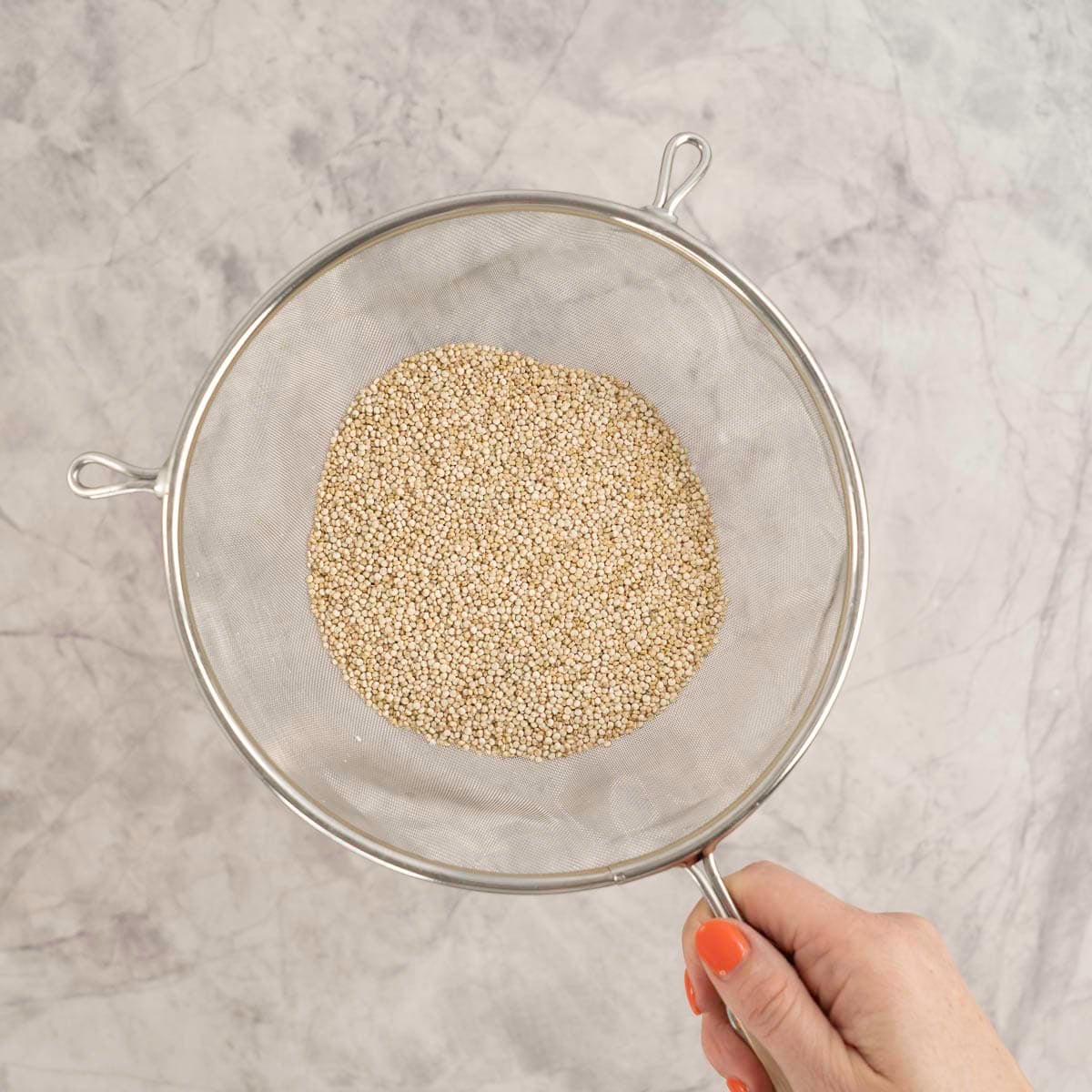 Hand holding a sieve with Quinoa inside.