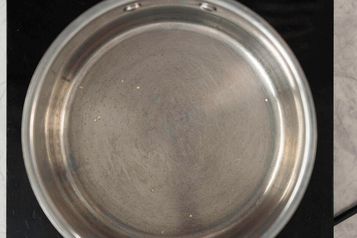 Pot on electric stove on bench top with just a couple of quinoa seeds in it.
