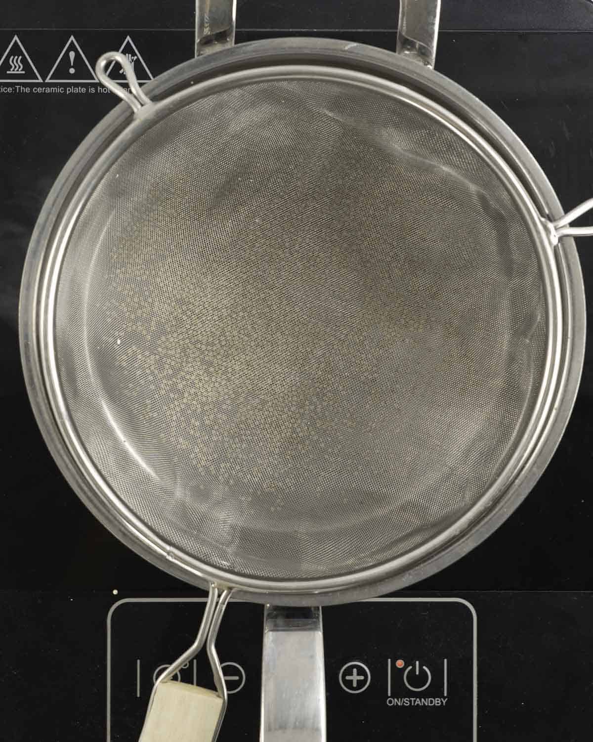 Sieve resting on top of a pot with quinoa on the bottom on electric stove.