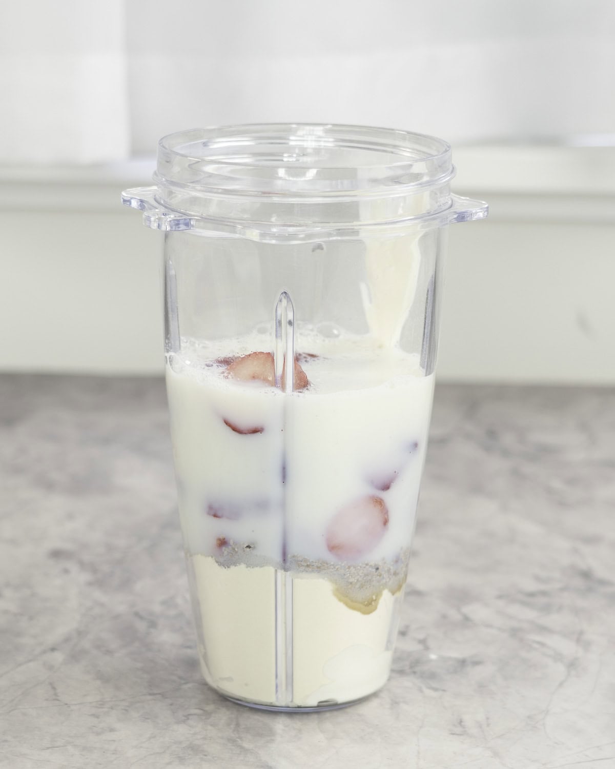 Blender cup with ingredients for strawberry shake inside.