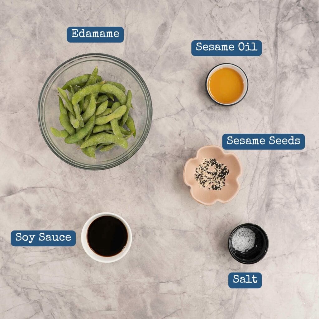 The ingredients to make air fryer edamame laid out in bowls on a bench top with text overlay.