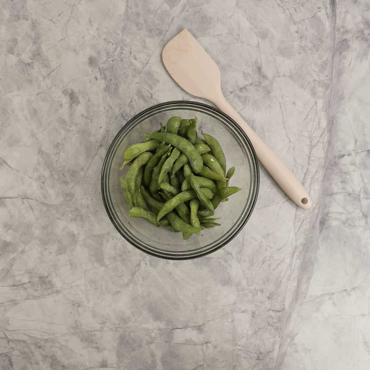 Frozen edamame in a glass bowl coated in oil.