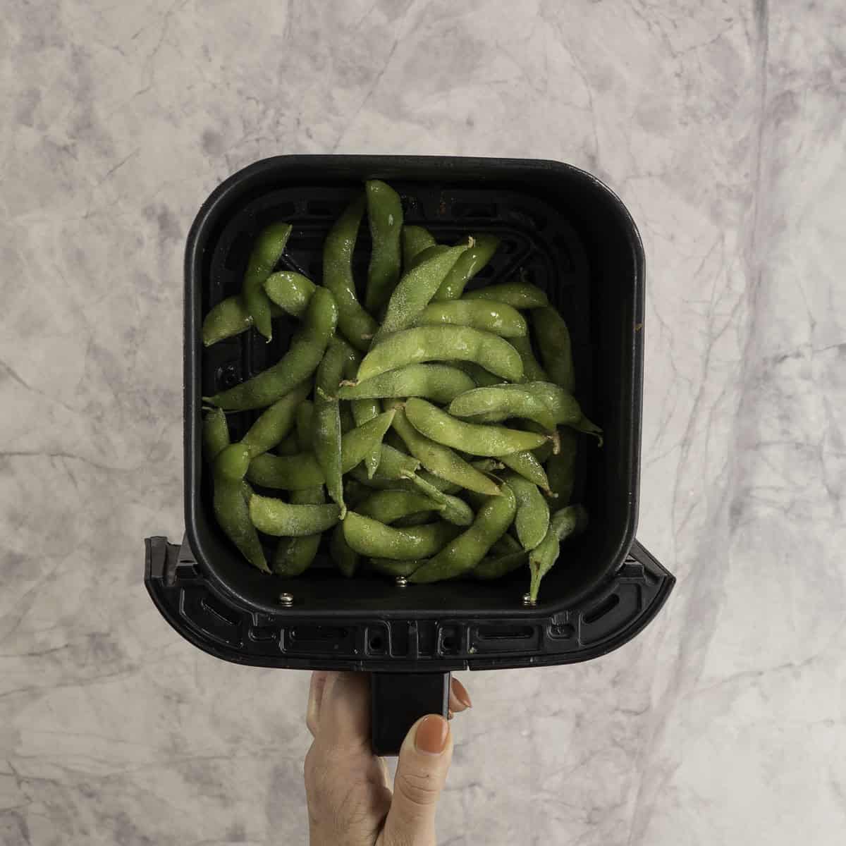 Frozen edamame in an air fryer basket.