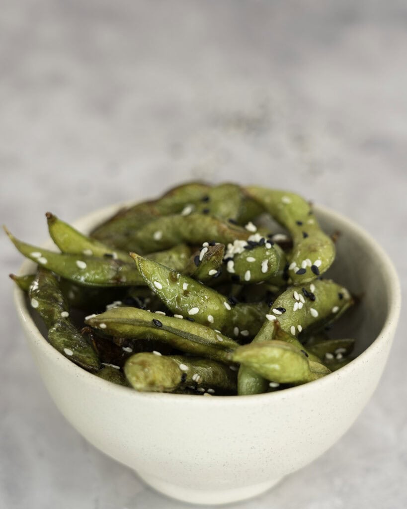 A bowl of edamame pods topped with seasoned black and white sesame.