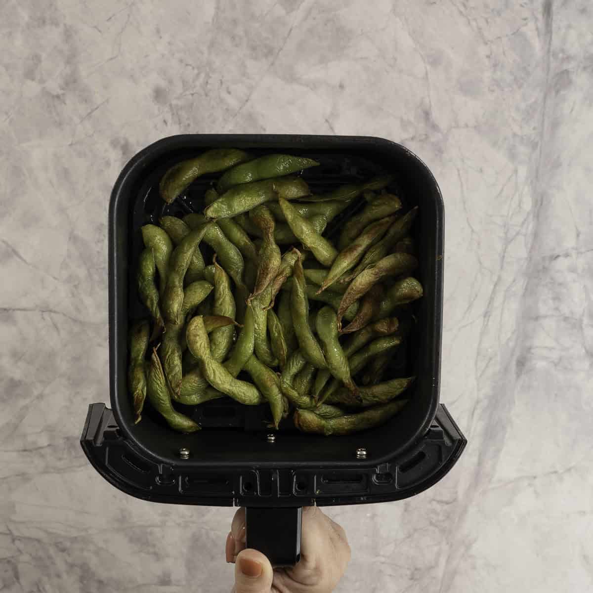 Cooked edamame in an air fryer basket, some lightly browned.