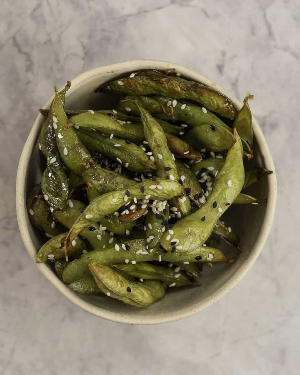 A ceramic bowl filled with browed edamame sprinkled with sesame seeds.