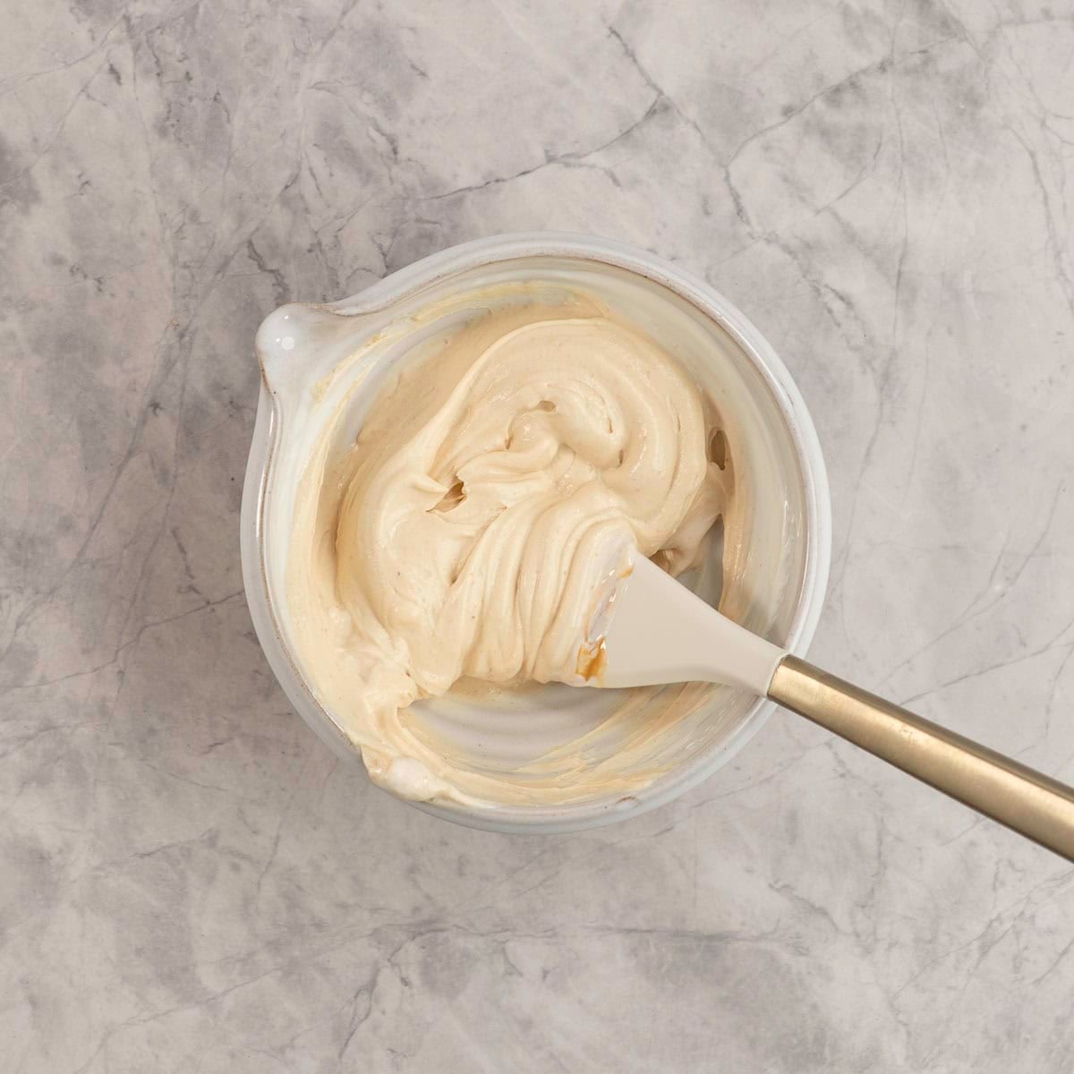 Peanut butter and yogurt in a white bowl mixed together with a spatula.