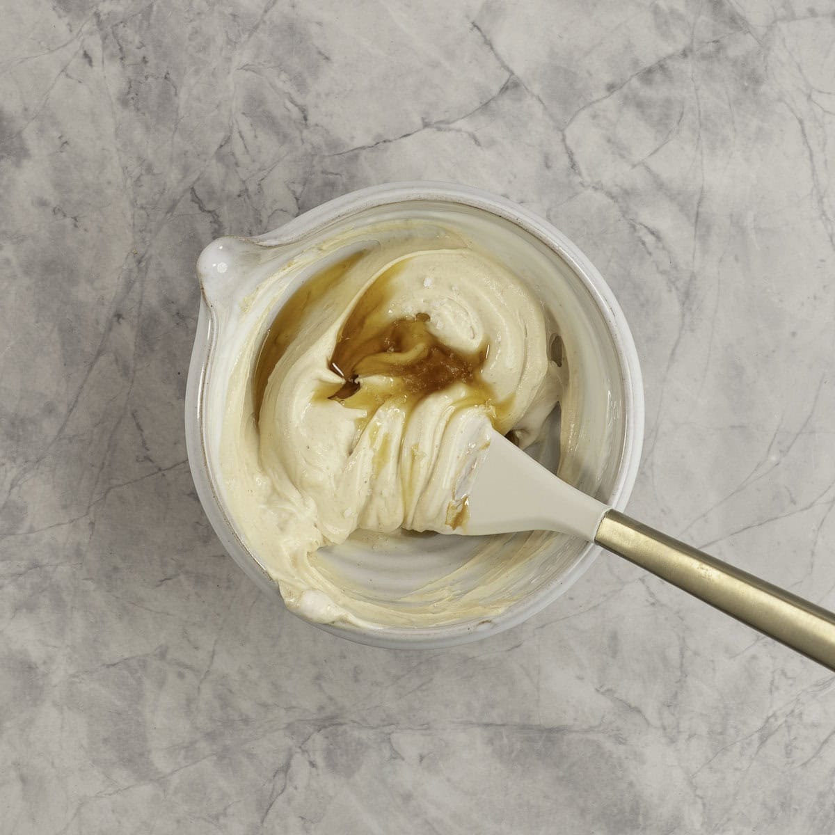Creamy mixture with maple syrup drizzled on top in a white bowl with a spatula inside.
