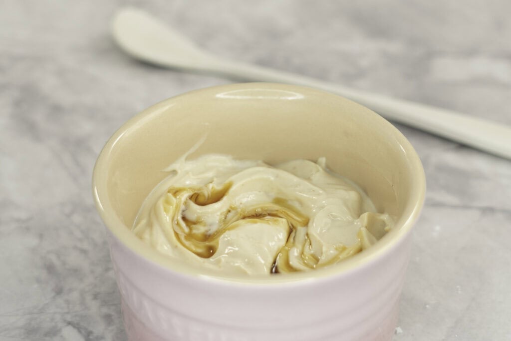 Creamy mixture with maple syrup drizzled on top in a small blush pink ramekin on marble bench top.