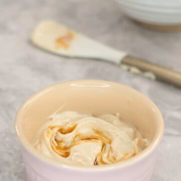Creamy mixture with maple syrup drizzled on top in a small blush pink ramekin on marble bench top.