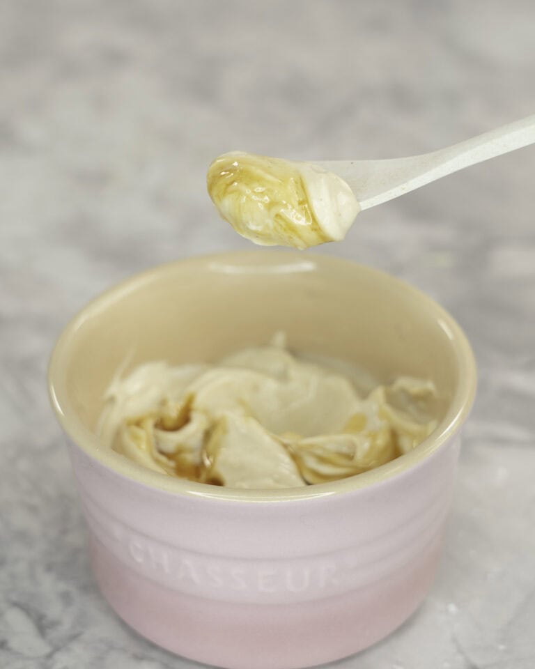 Creamy mixture with maple syrup drizzled on top in a small blush pink ramekin, white spoon taking a scoop out on marble bench top.