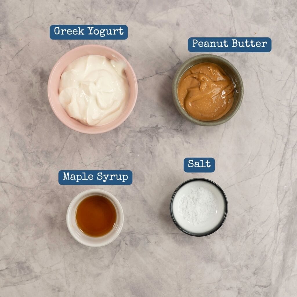 Ingredients for peanut butter yogurt on a marble bench top in small ramekins with text overlay.