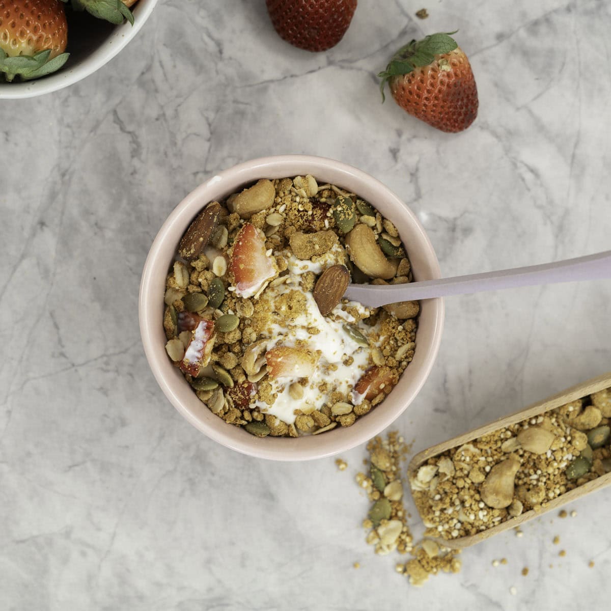 Small blush pink bowl with granola, yogurt and a spoon inside.