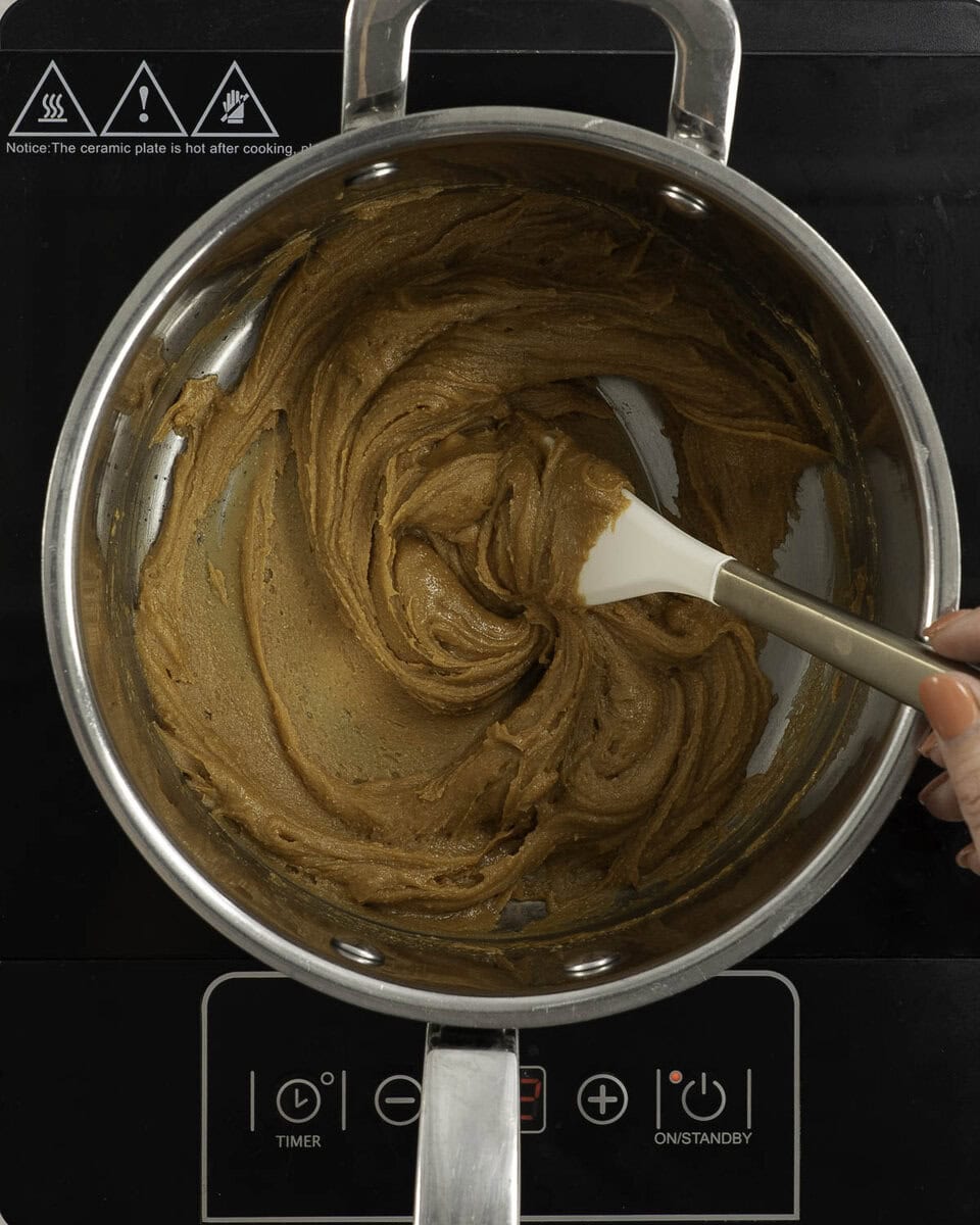 Peanut butter mixture in a large pot on stove top being stirred with spatula.