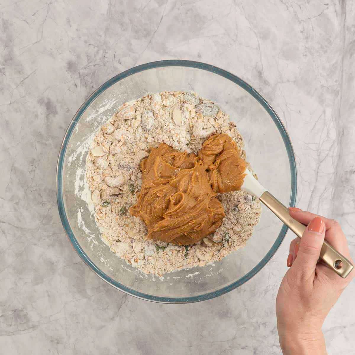 Dry ingredients for granola inside a large glass bowl with large dollop of peanut butter inside.