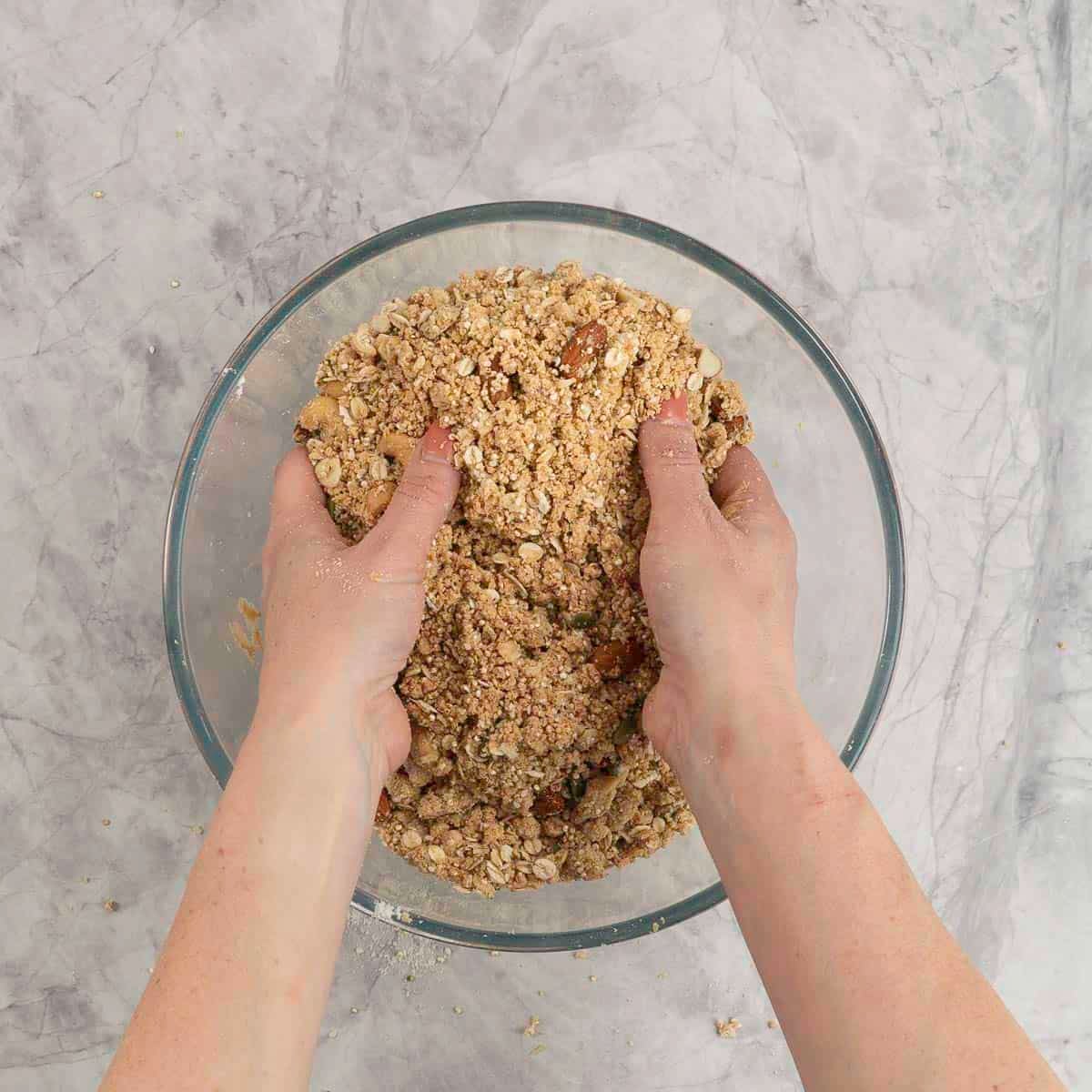 Large glass bowl with woman's hands mixing together homemade granola inside.