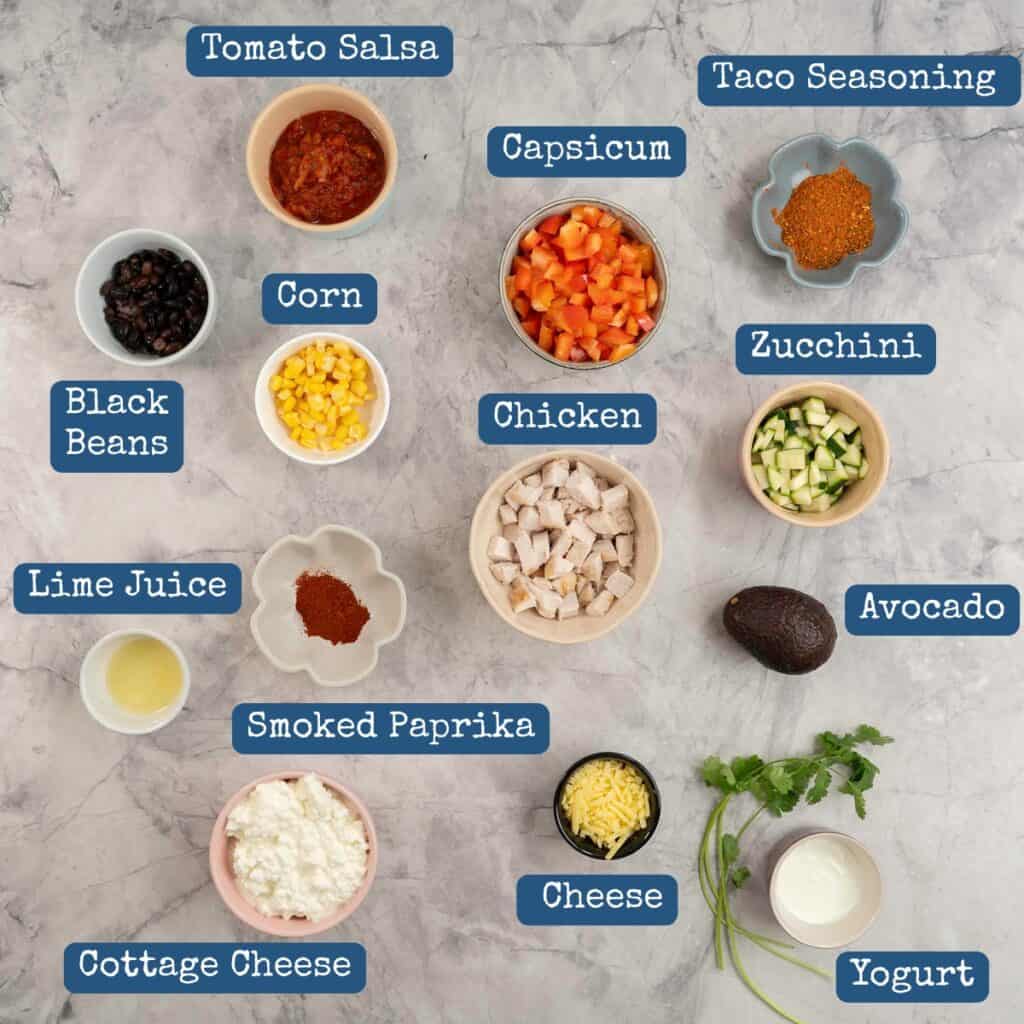 The ingredients to make Mexican chicken meal prep bowls laid out on a bench top with text overlay. 