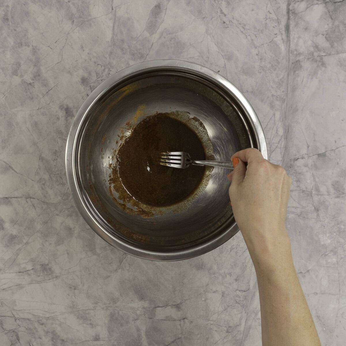 A mixing bowl with shawarma marinade, oil and spices, womens' hand mixing it with a fork. 