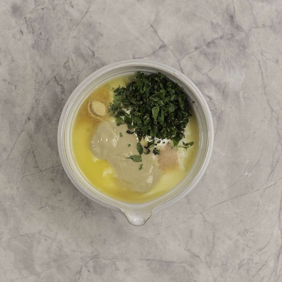 Yogurt, tahini, herbs in a mixing bowl, un-mixed. 