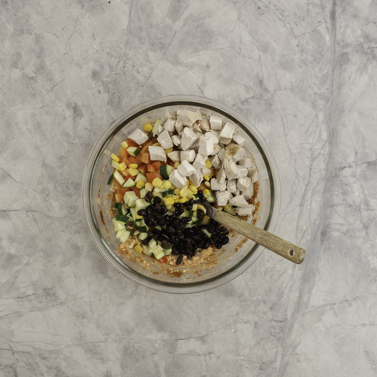 Diced  cooked chicken, black beans, corn kernels chopped bell peppers and diced zucchini on top of a cottage cheese mix in a bowl. 