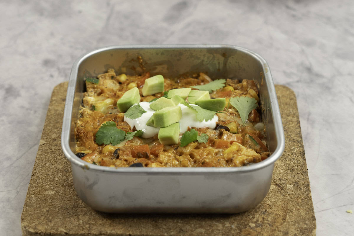 Enchilada in a stainless steel lunch box with yogurt and diced avocado on top. 