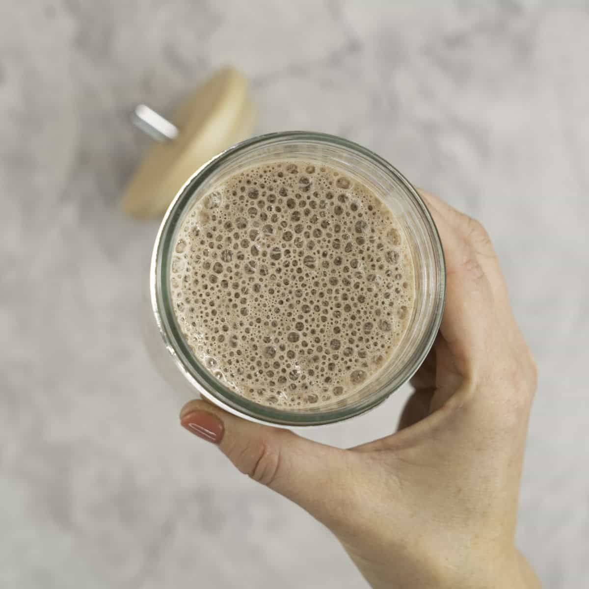 Womans hand holding a tall glass with smoothie inside.