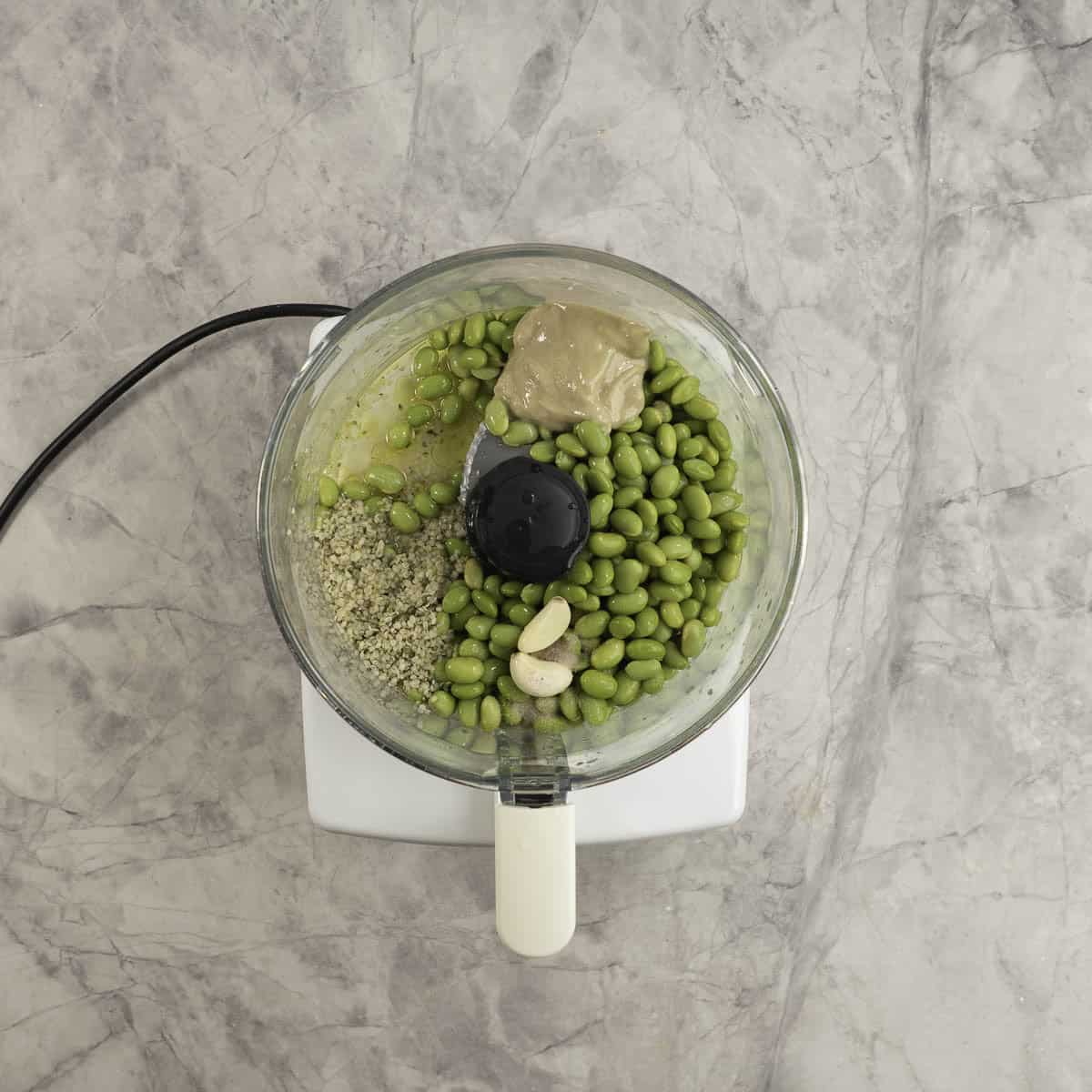 Ingredients for hummus inside a food processor on a marble bench top.