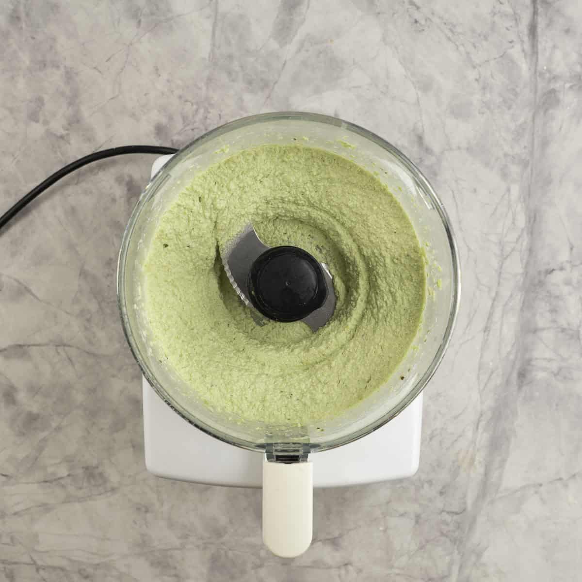 Food processor with hummus blended up to a smooth consistency inside.