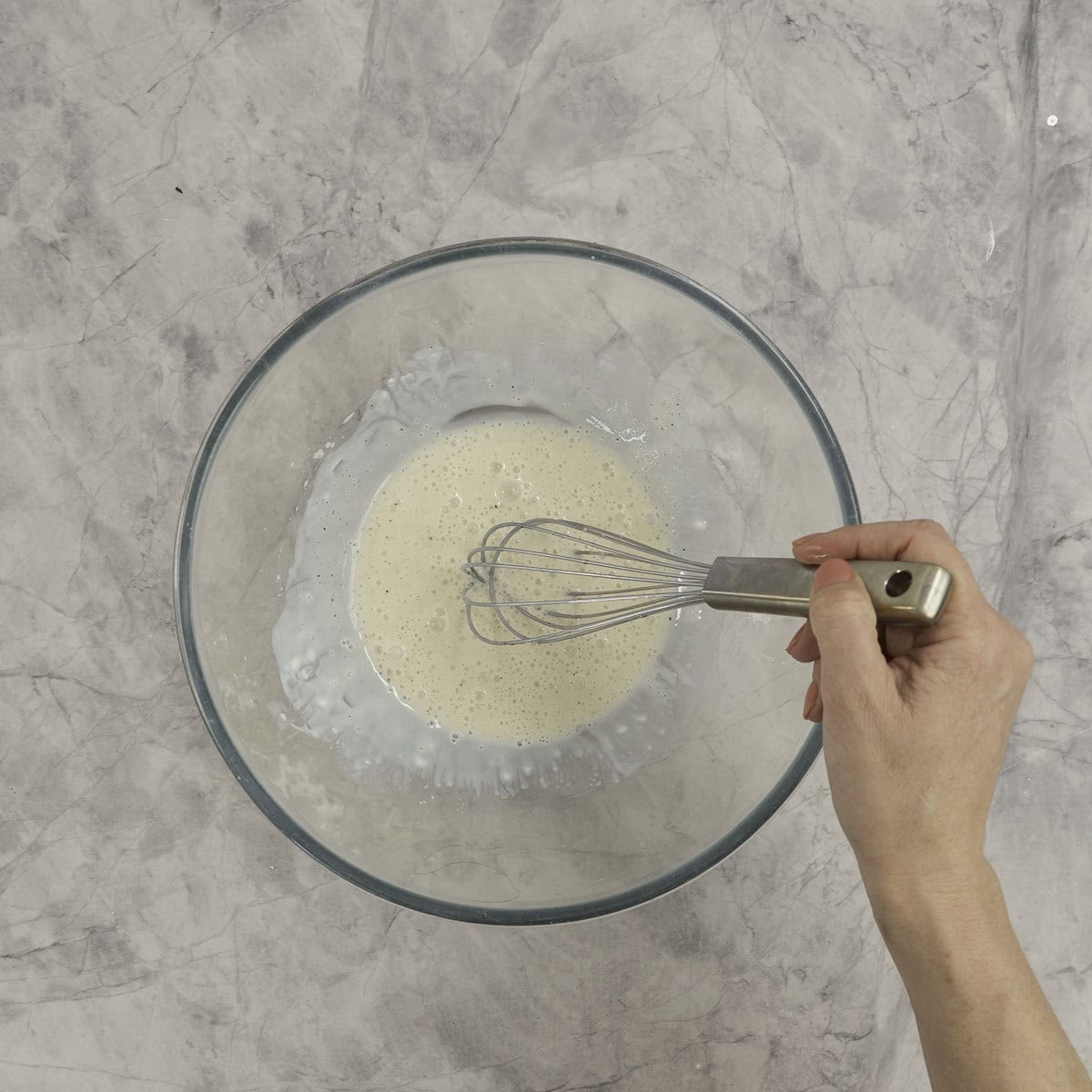 Creamy salad dressing whisked together in the bottom of a large glass bowl, hand with whisk visible. 