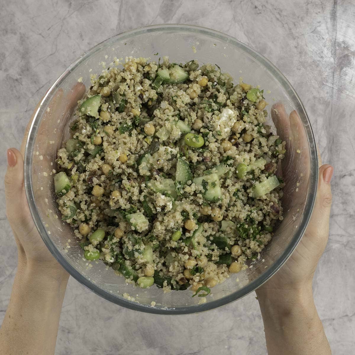 Womans hands holding a large glass bowl with salad inside.