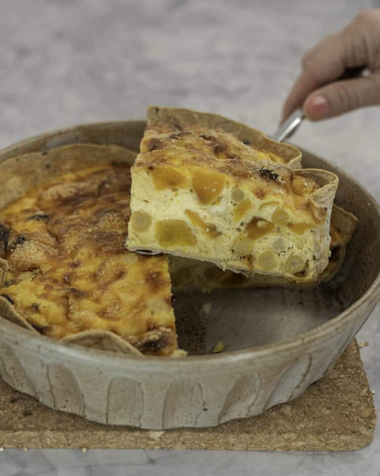 Womans hand holding a serving of quiche up out of ceramic baking dish.
