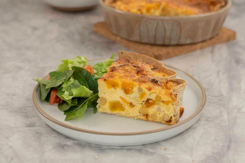A serving of quiche on a dinner plate with a portion of salad.