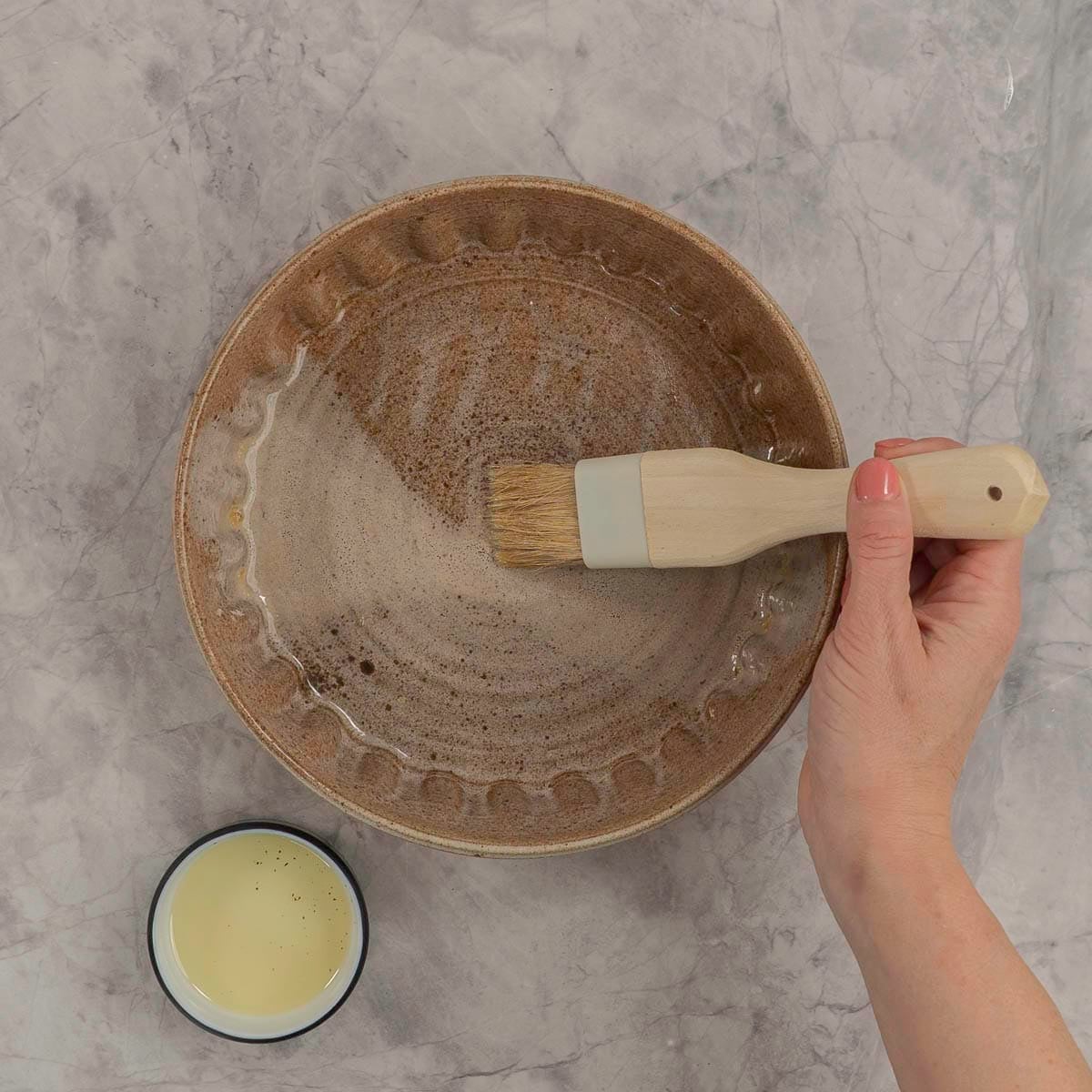 Woman using a pastry brush to coat baking dish with oil.