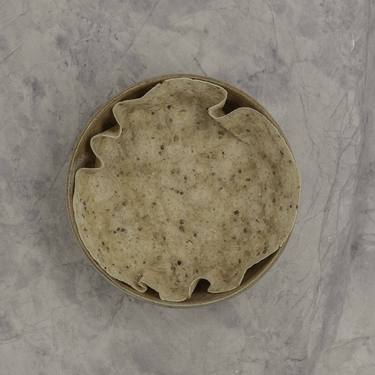 A tortilla wrap lining a round baking dish.