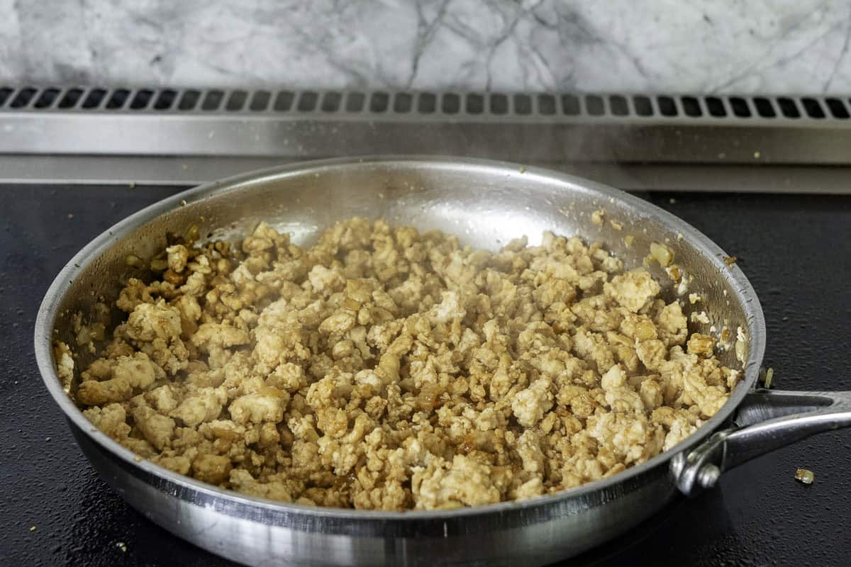 Chicken mince beginning to carmelise in a stainless steel pan on a stove top. 