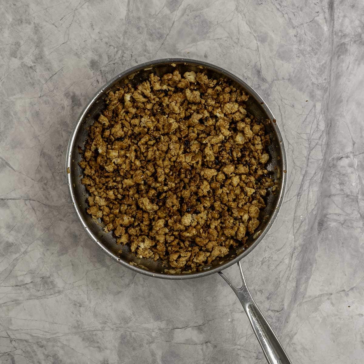 Browned chicken mince in a sauce pan on marble benchtop.