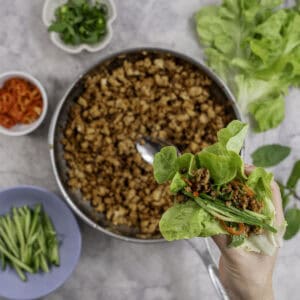 Woman's hand holding a piece of lettuce with mince, cucumber slices and chilli slices inside.