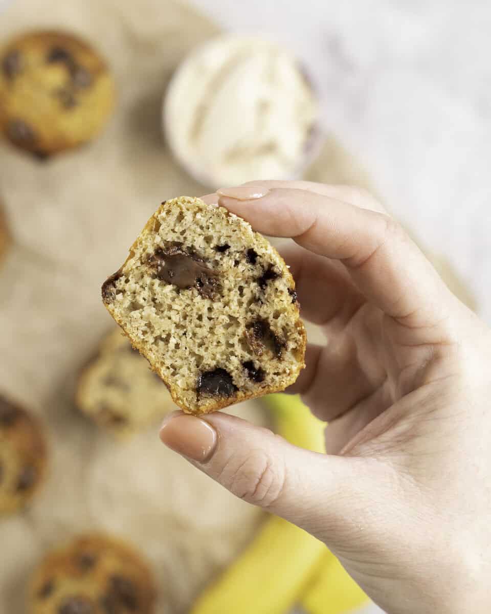 Womans hand holding a muffin cut in half showing fluffy inside with melted chocolate chips.