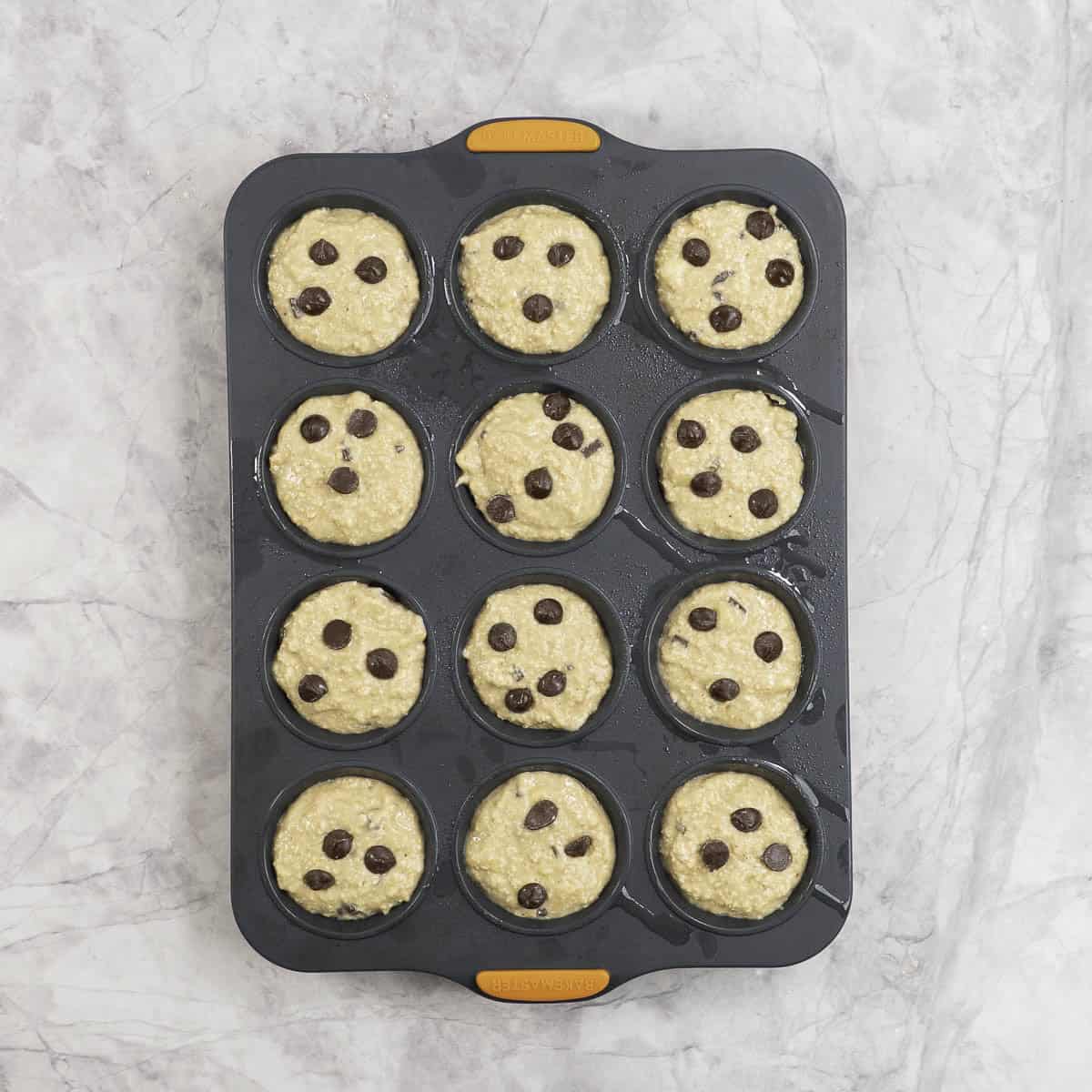 12 tray muffin tin with muffin batter and chocolate chips sprinkled on top.