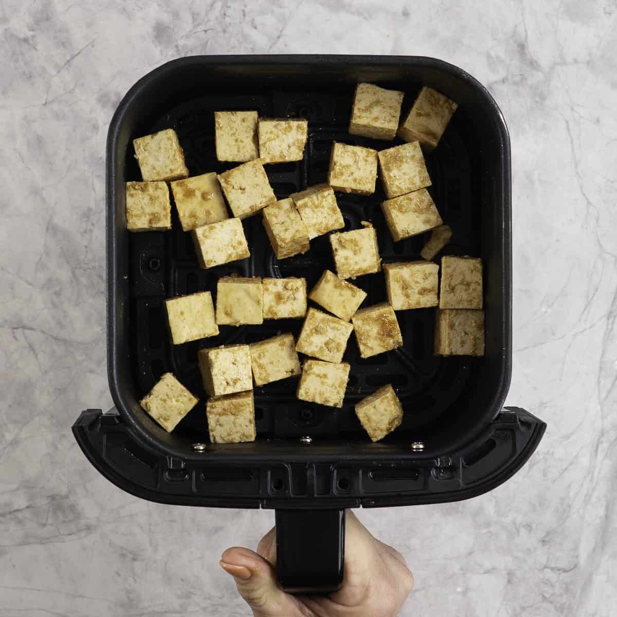 Marinated tofu pieces cut into small cubes in the tray of an air fryer.